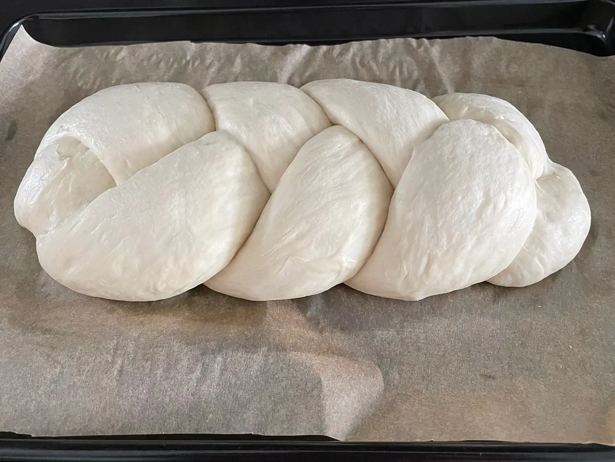 Cover the plaited dough with a damp tea towel again, or a piece of cling film. If using film, I sometimes use clothes pegs around the edges of the tray to help hold it in place. Put it back in the cupboard, and let it prove again for another hour. Again, if you leave it for a little longer, it’s not a disaster. Start heating your oven to 200℃ / 180℃ fan about 15 mins before you intend to bake.
