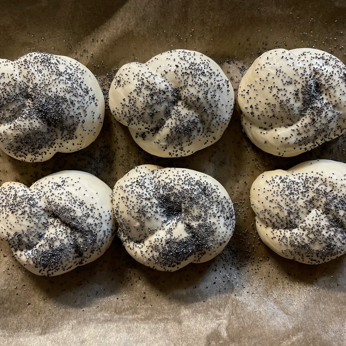 Once they’ve done their second prove, your knots will now be looking nice and fat. Carefully remove the cling film (it might stick a little), then brush them either with beaten egg, or with a little milk. Sprinkle them with a generous dusting of poppy seeds.
