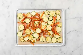 Préchauffez le four à 200°C. Détaillez la courgette en fines rondelles. Coupez le poivron pointu en deux, épépinez-le, puis taillez-le en lanières. Disposez les rondelles de courgette et les lanières de poivron sur une moitié de la plaque de cuisson recouverte de papier sulfurisé. Arrosez-les avec, par personne : 1/2 cs d'huile d’olive, 3/4 cc d’épices du Moyen-Orient. Salez et poivrez.