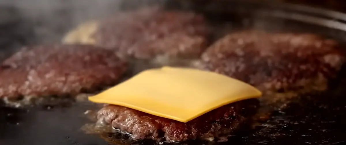 Scrape up the seared patty and clip them Add a slice of cheese to the top Add another patty on top of the cheese so they stick together