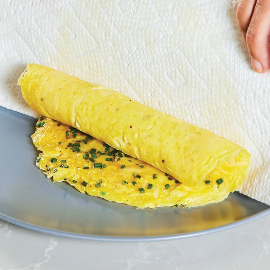 Heat skillet over low heat for 20 seconds, uncover, and, using heatproof rubber spatula, loosen edges of omelet from skillet. Place folded square of paper towel onto warmed plate and slide omelet out of skillet onto paper towel so that omelet lies flat on plate and hangs about 1 inch off paper towel. Roll omelet into neat cylinder and set aside. Return skillet to low heat and heat for 2 minutes before repeating instructions for second omelet starting with step 2.