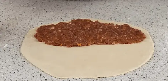 With a rolling pin roll out a ball of dough as thin as possible. Put filling on half of it and make it flat with your hands.