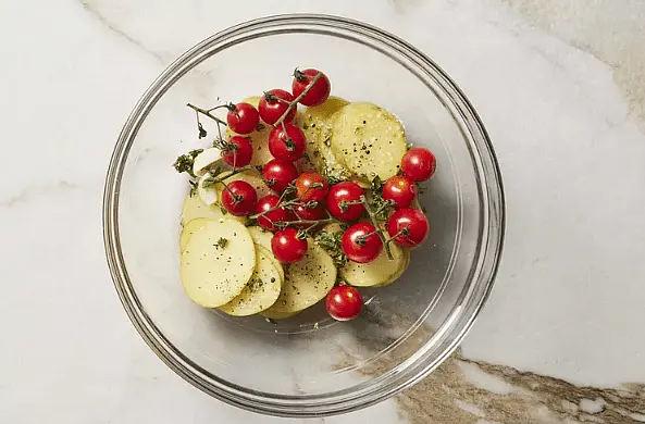 Preheat oven to 425°F. Toss together potatoes, tomatoes, garlic, oregano, 1 tablespoon oil, and 1/2 teaspoon salt. Season with pepper.
