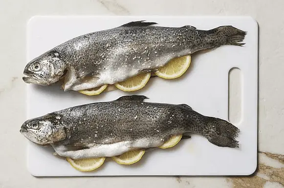 Rub fish with remaining 1 teaspoon oil, dividing evenly. Season inside and outside of fish with remaining 1/2 teaspoon salt; stuff with lemon slices.