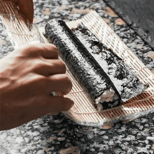 Add some of the rice to a nori sheet, and really press the rice to the nori before you roll, so your roll is not loose and falls apart later. Add one sausage on top of the pressed rice, and roll. Make as many rolls as you like / till you finish your sausages.