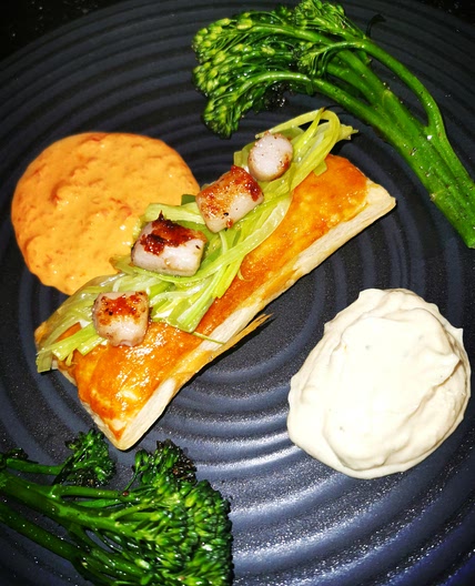 Scallops shallow fried in cocoa butter on a leek cream filled puff pastry, with garlic sauce and sweet pepper sauce