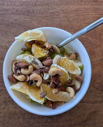 Mixed unsalted nuts and chia seeds with oranges, green grapes, green and red apples, strawberries, and Greek yogurt