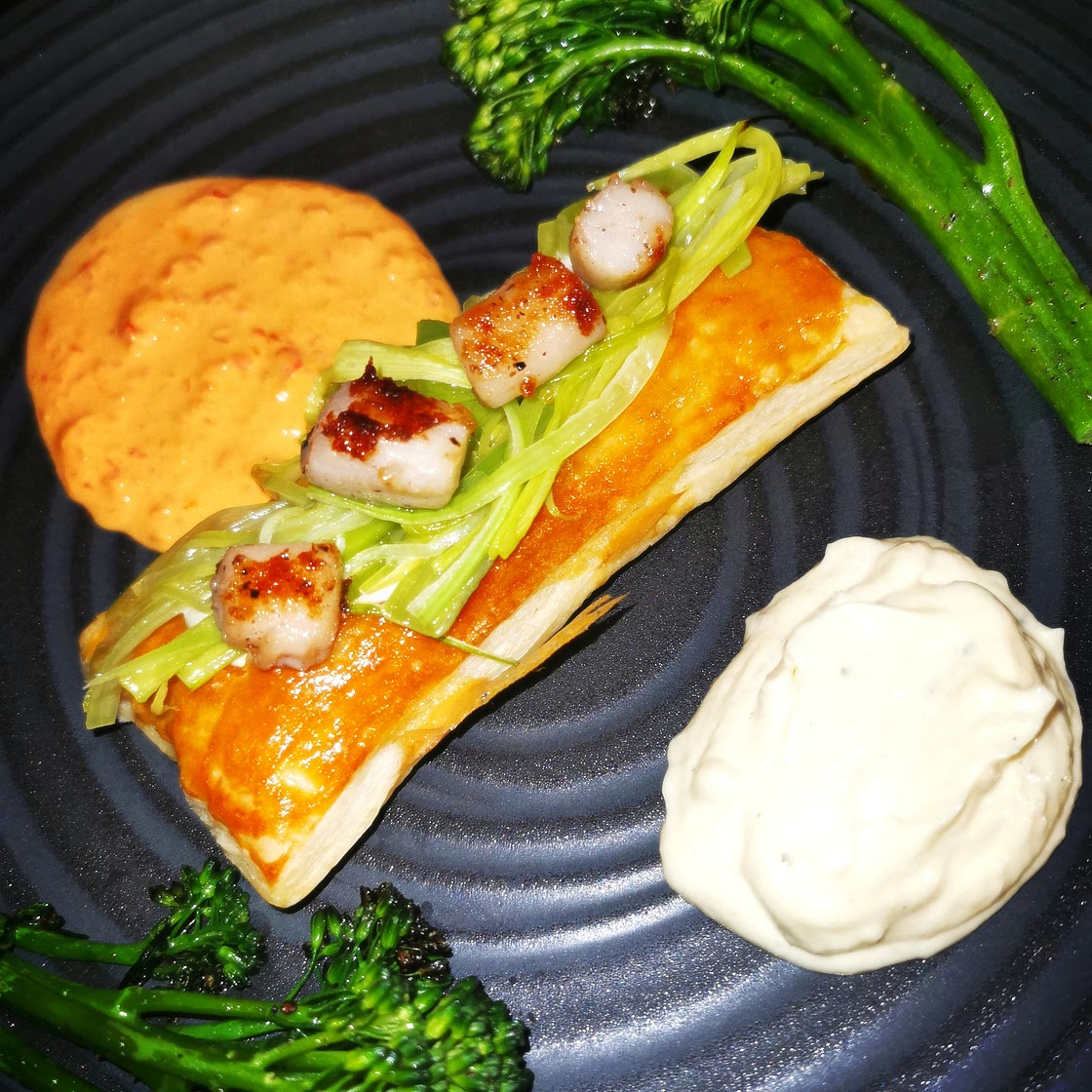 Scallops shallow fried in cocoa butter on a leek cream filled puff pastry, with garlic sauce and sweet pepper sauce