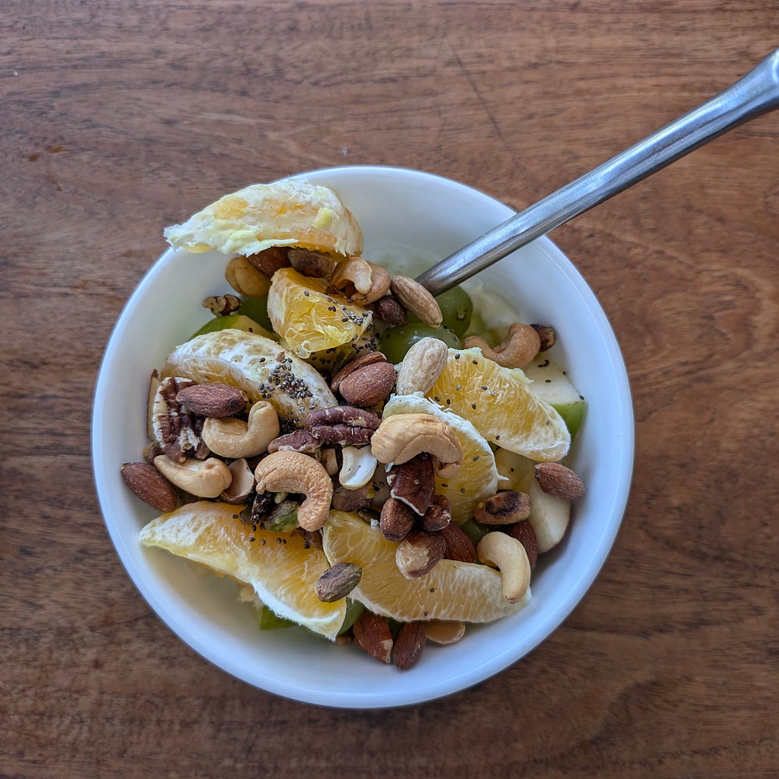 Mixed unsalted nuts and chia seeds with oranges, green grapes, green and red apples, strawberries, and Greek yogurt