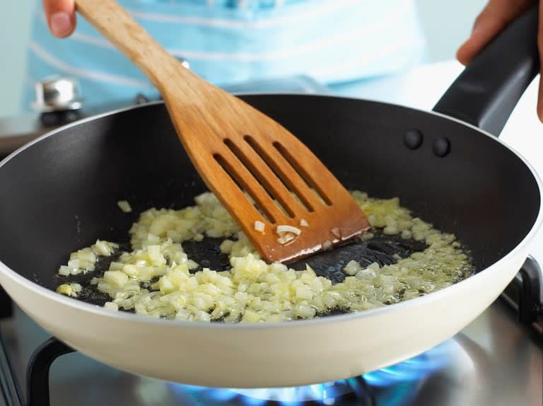 Während der Teig im Kühlschrank entspannen darf, bereiten wir die Liaison bzw. die Füllung vor. Dazu schälen wir die Zwiebel und waschen den Lauch kurz ab. Beides schneiden wir anschließend in feine Stücke bzw. Ringe. Den Speck schneiden wir in kleine Würfel. Sobald wir alles geschnitten haben, erhitzen wir eine Pfanne und lassen den Speck darin aus. Dazu geben wir die Zwiebel und dünsten sie an.