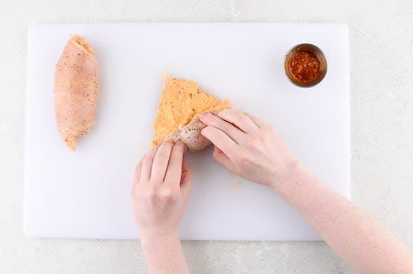 Stuff the Chicken
Pat chicken dry. Cover chicken with plastic wrap and use a heavy object to pound to an even 1/3" thickness. Remove plastic and season both sides with a pinch of salt and pepper. In a mixing bowl, mash softened cream cheese and half the red pepper pesto (reserve remaining for sauce) until combined and smooth. Spread cream cheese-pesto evenly on chicken. Starting from the widest part, roll chicken into a pinwheel, then place seam side down. Wipe bowl clean and reserve.
