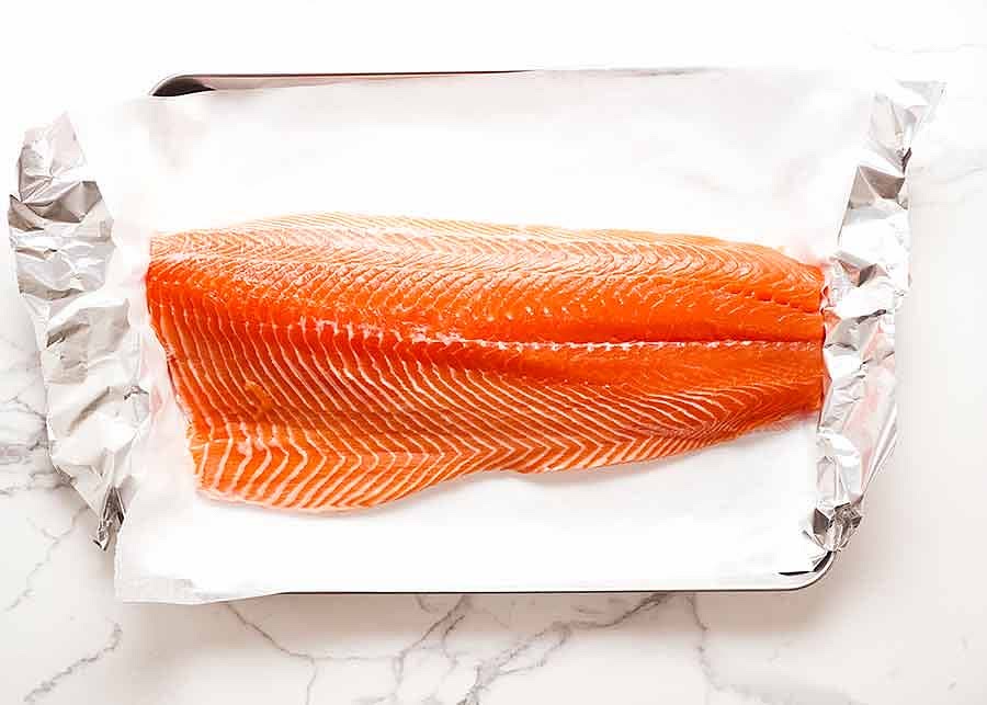 This is one side of a whole salmon. It should not be flavoured or pre-marinated in any way. If frozen, thaw thoroughly overnight in the fridge covered, and then pat dry very well (frozen fish gets watery); Skin on – for easier handling. Once cooked, the skin will hold the salmon together. Without it, there’s a higher change the flesh flakes open when transferring to the tray. Interestingly, I have never seen a side of salmon sold without skin – this may well be the reason; and Bones removed – Your fishmonger should have already done this, but just double check. Run your fingers across the surface, especially along the mid-line (where the spine was) where pin bone culprits sometimes hide. Check the belly section carefully too. If there are bones, use fish boning tweezers or just personal grooming tweezers to pull them out (pinch and yank with conviction!). Clean small pliers also work.