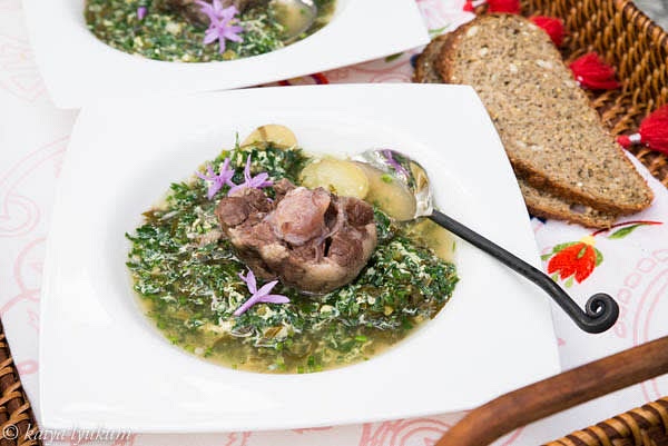 When potatoes and parsley root are ready, add greens and oxtail segments, and turn heat to high. Crack raw eggs in a bowl. When your soup starts boiling, drop raw eggs and mix — they will turn into yellow and white threads. Turn off the heat and serve piping hot. Garnish each portion with an oxtail segment and chives flowers.