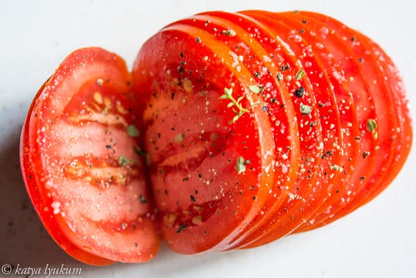 Wash, dry, and slice tomatoes, not cutting through the end. Season them with salt, pepper, and fresh thyme leaves.