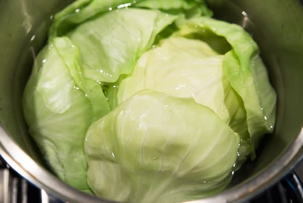 Place cored cabbage head into simmering water, bottom-up. In 2-3 minutes, the first 3 outer leaves will become soft and loose. Remove them from the pot and place them in a colander to drain. Continue with the next layer. It takes about 10 minutes to soften all cabbage leaves, layer by layer.