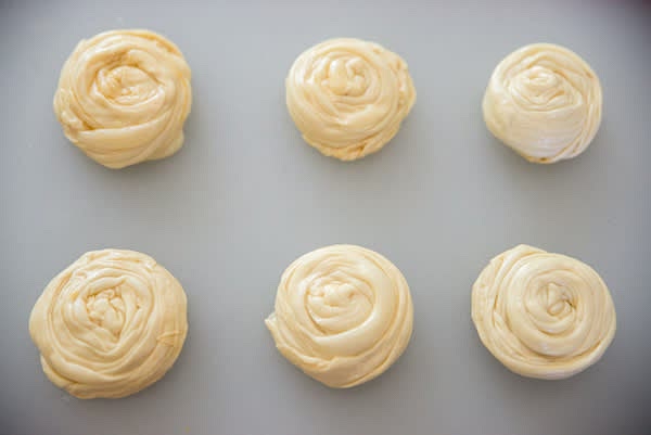 Work with one portion of the dough at a time. Keep the rest covered with plastic wrap. Lightly grease working surface with melted ghee. Use a rolling pin to stretch each portion of the dough paper-thin. Lightly brush it with more ghee. Gently peel it from the working surface and make 1" wide accordion fold. Roll folded dough into a spiral with the end tucked. Grease your working surface again and repeat with the next portion of dough.