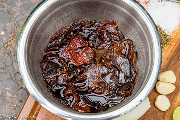 Prepare dry peppers. Remove stems, veins, and seeds. Cut them into small pieces, place them in a bowl, and pour hot water over them. Submerge them in the water and leave them to reconstitute for 20-25 minutes. Strain and reserve the water.