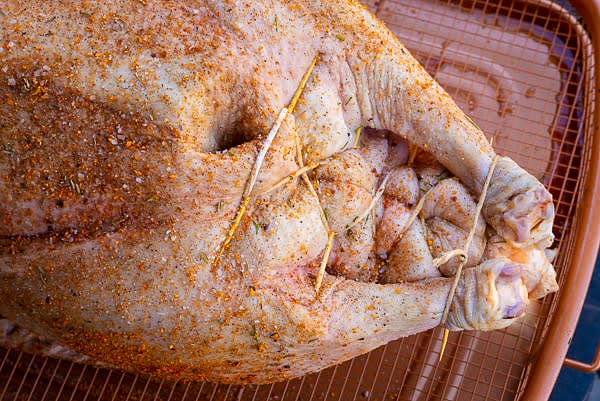 Inspect the bird for any feathers. Remove those the processors might have left. Place the goose backside up and tie the wings, so they stay close to its body. Turn the bird breast up and stuff the cavity with prepared stuffing. Use toothpicks to thread the skin's edges above the tail and use the culinary thread to connect them, legs, and tail, as shown in the picture.