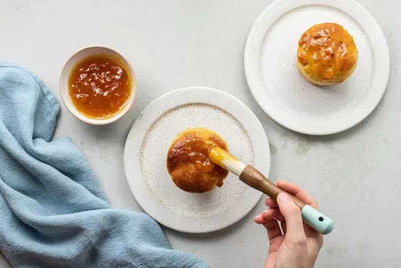 Carefully transfer each baba onto a dessert plate and brush with a generous amount of warmed apricot preserves.