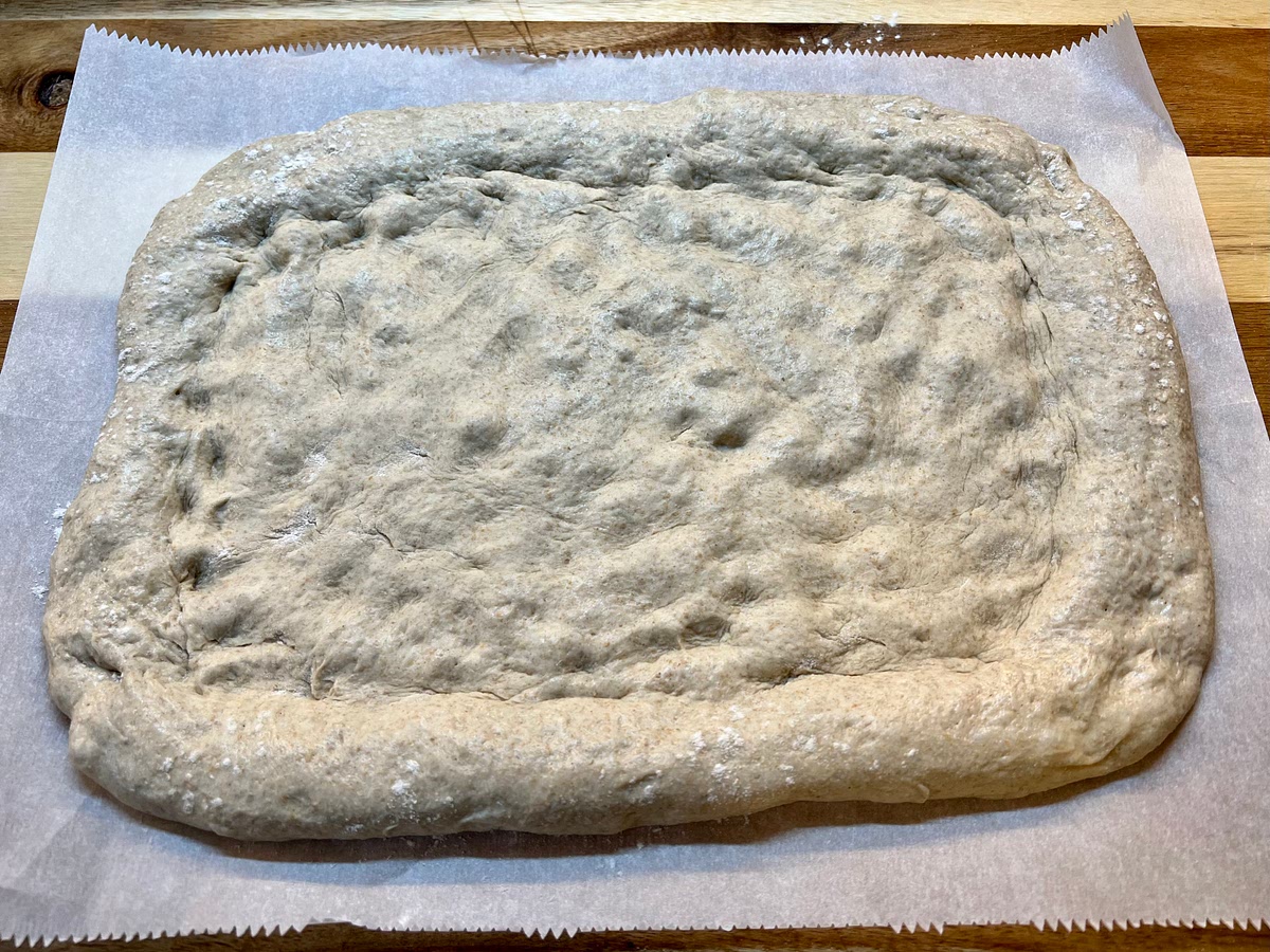 Use your hands to press a ball of dough into a circle or rectangle on a floured piece of parchment. Use more flour as needed to prevent sticking. (If you find the dough difficult to shape into a pizza crust, let it to rest on the counter for 15 minutes in order for the gluten to relax.)