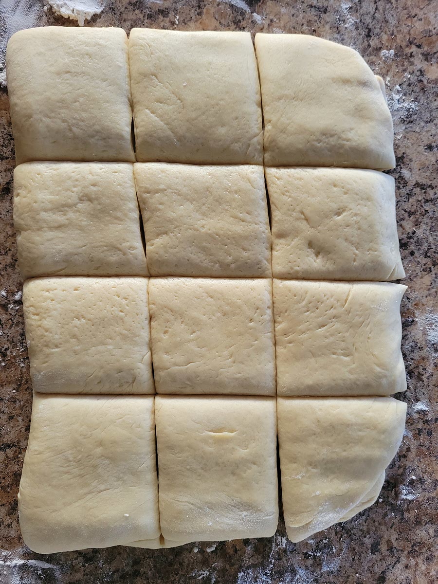 FOLD THE DOUGH IN HALF, SO IT’S NOW ABOUT 1-INCH THICK, ROLL OVER THE DOUGH A LITTLE BIT TO SEAL THE TWO HALVES TOGETHER. CUT THE DOUGH INTO APPROXIMATELY 2-INCH SQUARES.