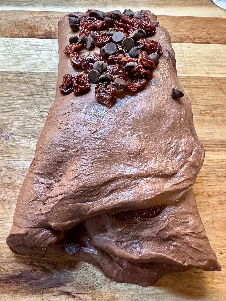 Gently stretch the dough the long way, and fold up 1/3 of that length. Sprinkle the remaining inclusions, then fold it over to make a rough square.