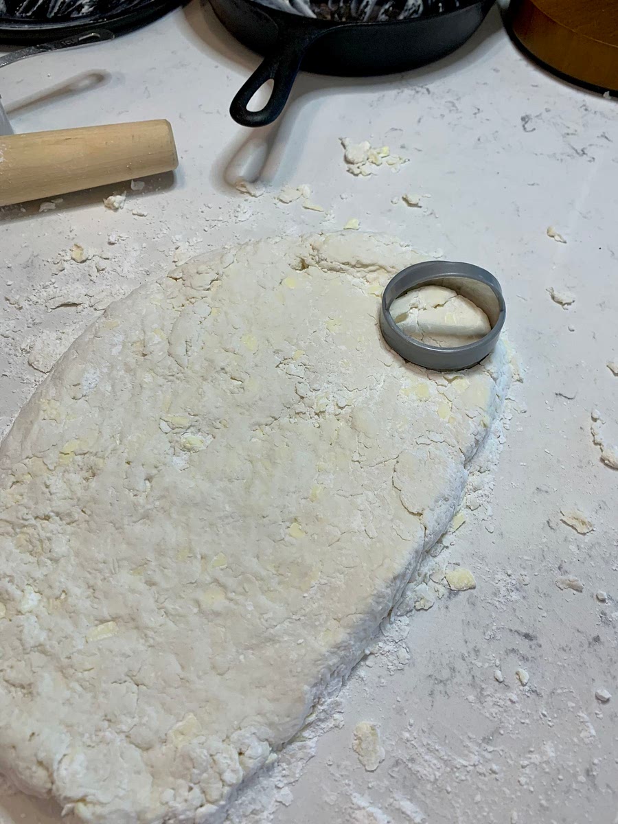 Preheat oven to 475 degrees. Butter the cast iron skillet. Stir ingredients 10-15 times, being careful to not over mix. Handling the dough too much makes tough biscuits. Turn the sticky dough onto a floured surface. Roll the dough 1-2 times, again being careful to not over mix or overwork. Cut the biscuits out and place in the pan with sides touching each other. This will allow the biscuits to rise to their full potential. Bake for 15 minutes.