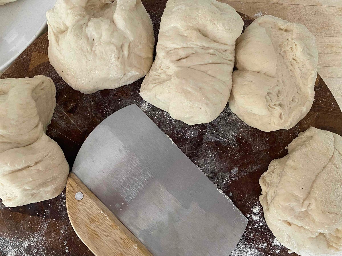 Remove the dough from the bowl and divide equally into 6 portions. On a chopping board sprinkle a little flour and if you have some, semolina. With your hand knead again for about a minute to form a firm ball of dough.