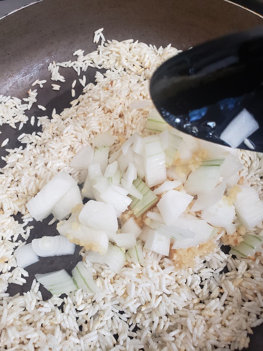 Una vez dorado el arroz, añadir el ajo y la cebolla picada, freír por 3 minutos más.
