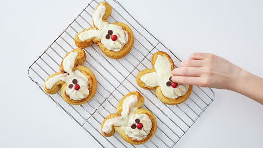 Spread frosting on warm rolls. On each bunny, place two chocolate chips for eyes, 1 red baking chip for nose and 2 almond slices for teeth. Serve warm.