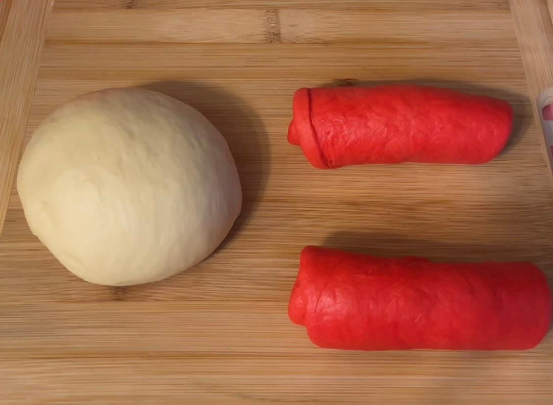 Split the coloured dough into 2 pieces. Roll out each piece into an oval shape then use the palm of your hands to roll it forward.