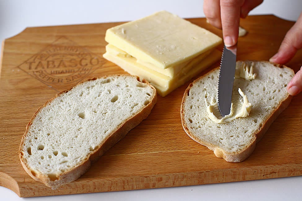 We put the pan with a lid on medium-low heat, let it heat up. While the pan is hot, spread two slices of bread with ½ of the spicy butter on both sides. Divide the cheese between the two slices of bread.
