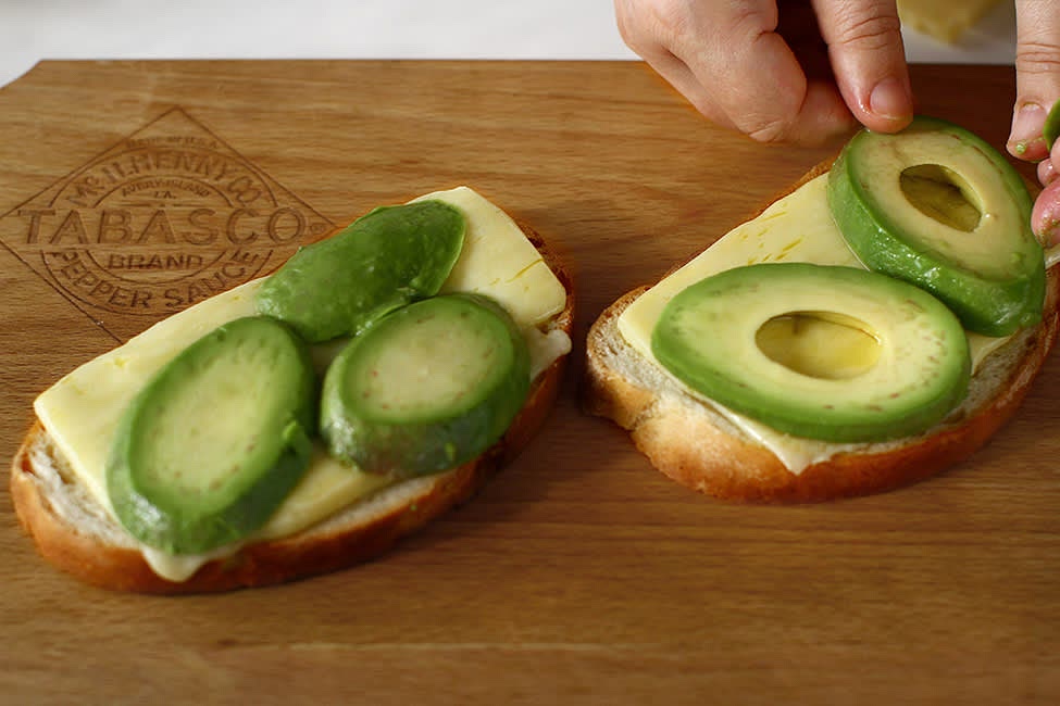 As soon as the eggs are done, they are removed from the pan. Take out the toasted bread with slightly melted cheese and place it on a chopper. Sprinkle the avocado slices with salt and place on top of the cheese bread slices.