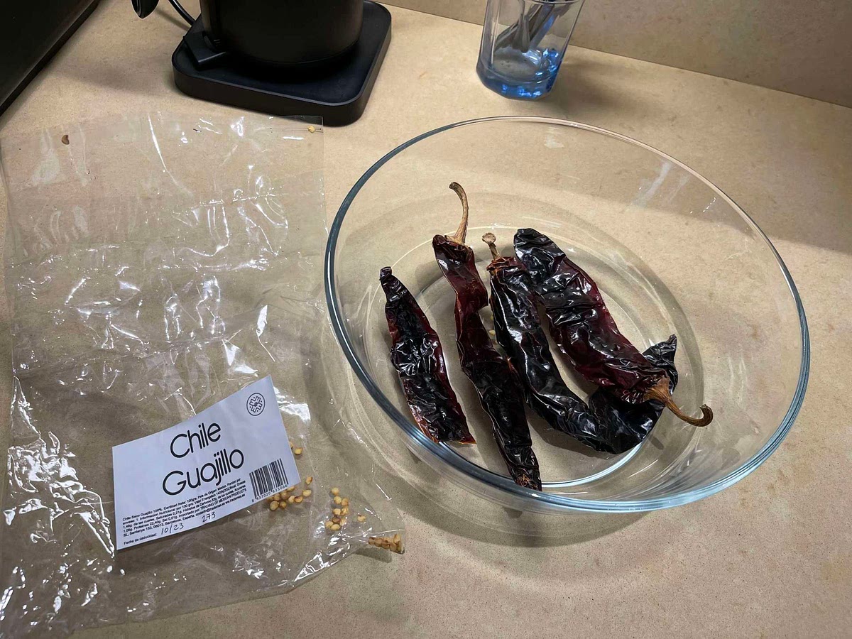 Reconstitute dried peppers by covering with hot water. Leave at least 15 min. Remove from hot water, split open each pepper, clean out seeds and ribs, retain water.