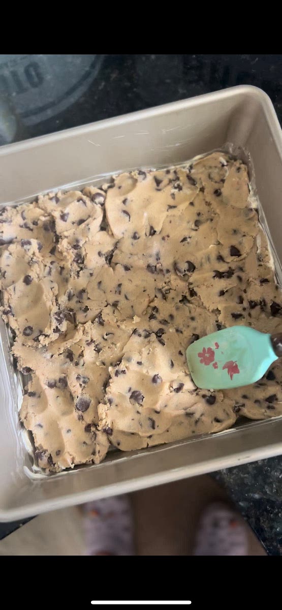 Spread the cookie dough evenly on the bottom of the prepared baking pan. You can press it down gently to create a solid base layer.