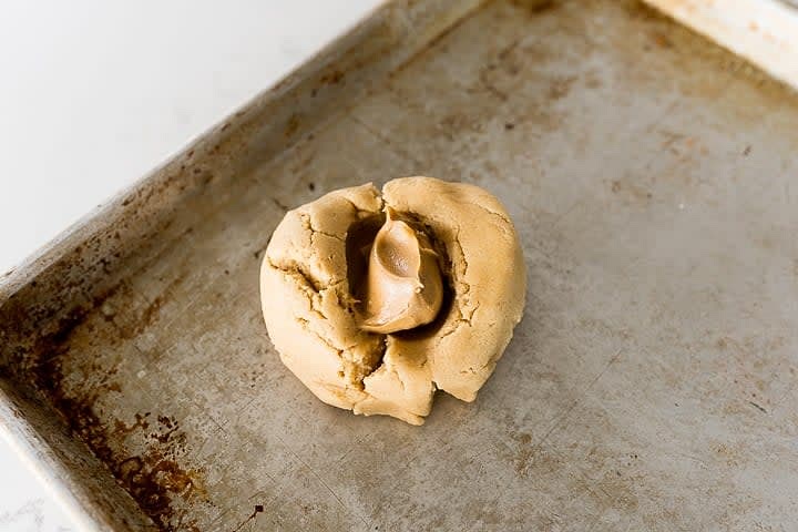 Coloca una porción de 1/2 cucharada de mantequilla de cacahuete en el hueco y cierra la galleta alrededor de la mantequilla de cacahuete. Aplana ligeramente la galleta con las manos para que se asemeje a un disco de hockey, y repite con el resto de las bolas de masa.