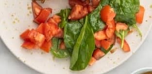 Add spinach to the bowl with tomatoes. Toss to combine. Divide onto two plates and serve.