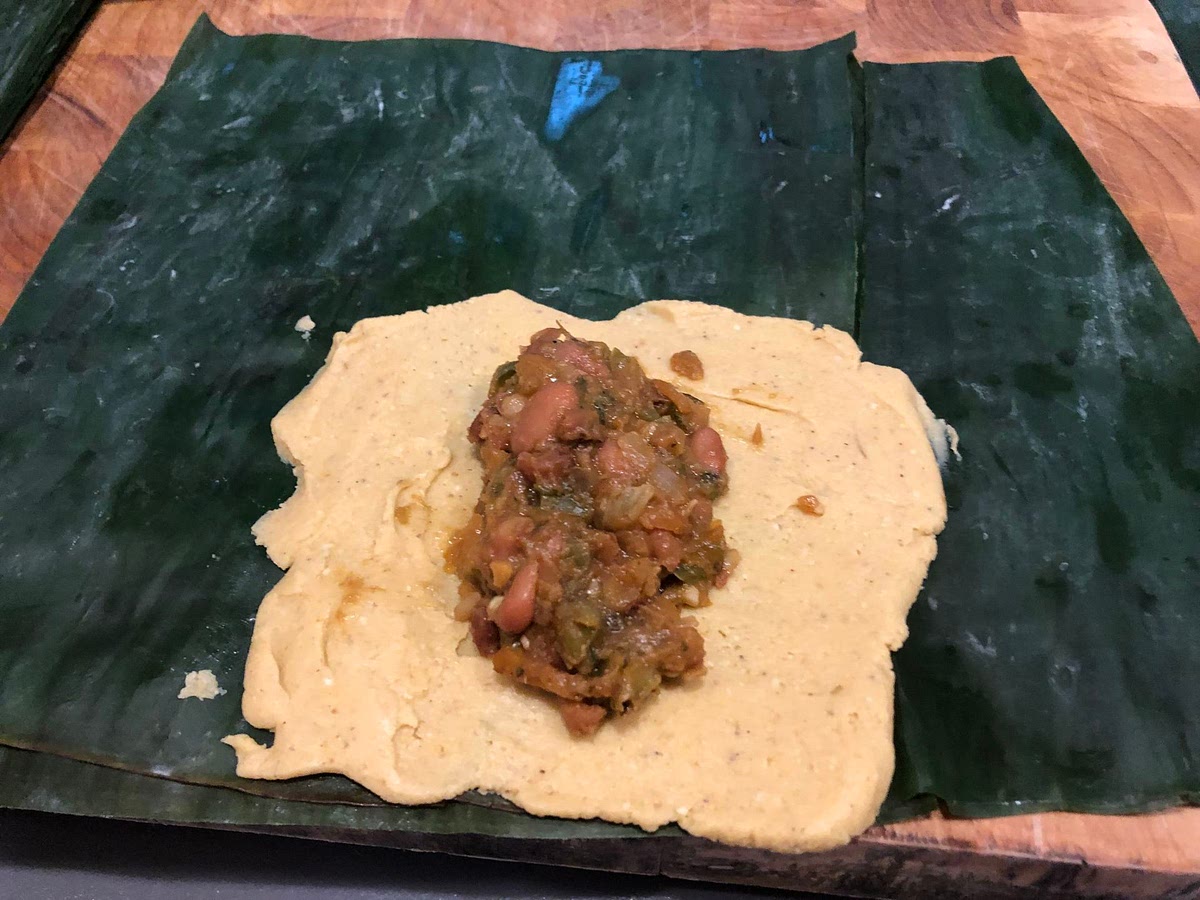 Now it’s time to wrap the tamales. Cut off the hard edge of the banana leaves, then unroll them and cut rectangles about the size of a laptop screen or a large iPad. Spread a dollop of dough on the flat side of the banana leaf, against one edge but about 1/2 to 2/3rds of the way down. A spatula would work for this, but I found my plastic rice paddle even better. Then spoon a heaped tablespoon of the cooled filling in the middle, leaving some room either side. Then bring the sides of the banana leaf in toward the centre so the masa harina mix folds over the filling - this is why the filling needs to be both sticky *and* non-stick. Trust me, when you do it, you’ll understand. If you’re lost, you may need to watch a YouTube video of these being made. Once it’s wrapped into a tube, fold the unfilled part of the banana leaf around to form the bottom of the tamale. Then tie it off, either with a strip of banana leaf, or with twine, like I did. When you’ve used up all your dough and filling, you’re done.