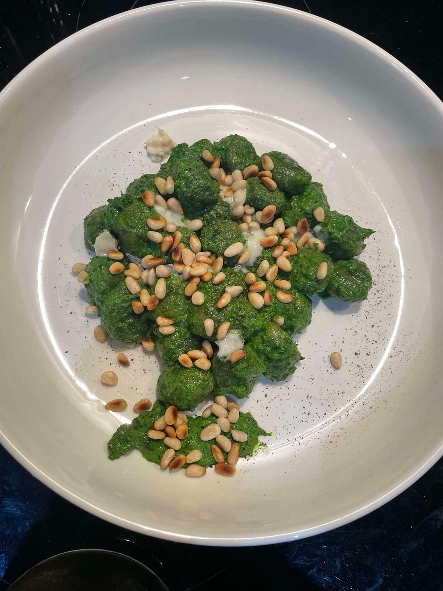 Mix the gnocchi with the green sauce and serve into bowls. Sprinkle the remaining blue cheese and pine nuts with black pepper.
