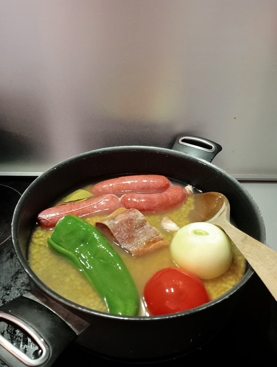 Echamos a la olla: la cebolla pelada pero entera, el tomate entero sin pelar con un tajo en forma de cruz en el culo, el pimiento sin pipos, los dientes de ajo sin pelar, las hojas de laurel, las lentejas, el hueso de jamón, la sal y los chorizos.