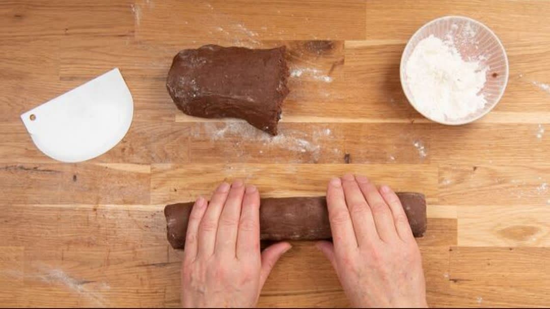 Bestäube deine Arbeitsfläche jetzt mit etwas Weizenmehl, teile den Teig mit einer Teigkarte in 2 gleich große Portionen und forme mit deinen Händen aus jeder Portion eine Rolle.