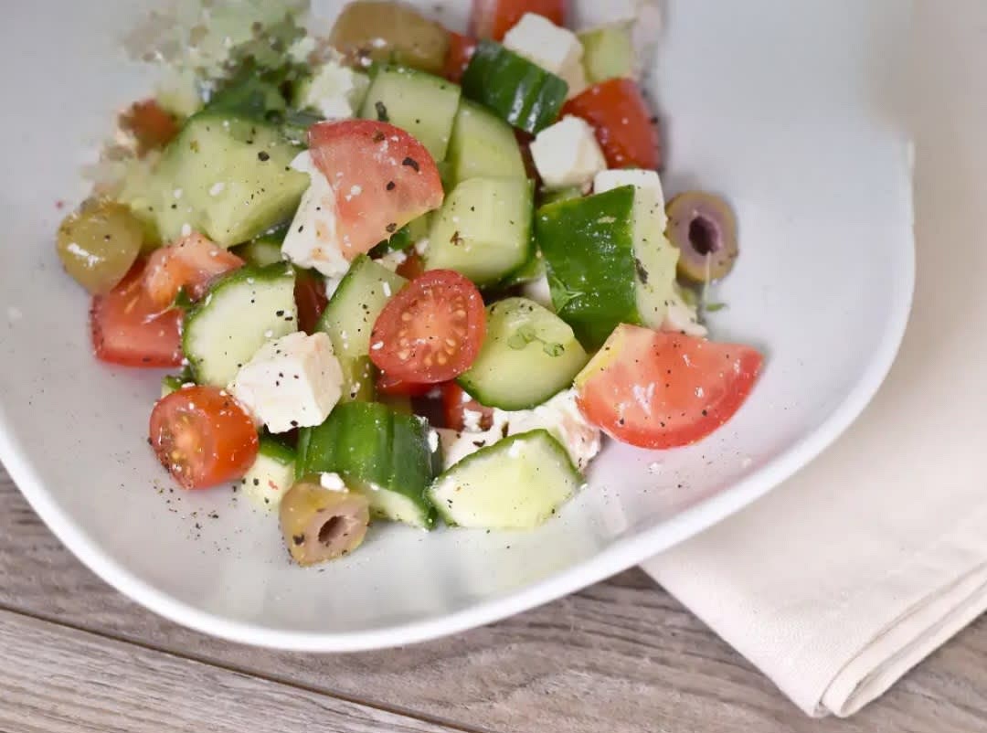 Salatgurke und Tomaten klein schneiden, die Oliven halbieren und in eine Schüssel geben.