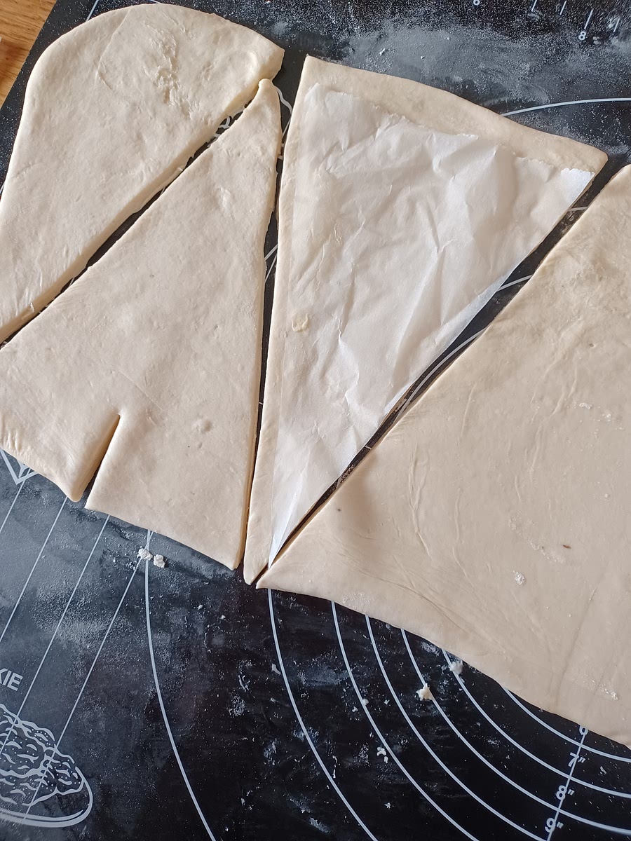 PrĂ©paration des croissants : Etaler la pĂąte (toujours dans le sens haut bas si les plis sont visibles face Ă soi). Tenter de faire un rectangle de 18/20cm de large (peu importe la longueur), dâune Ă©paisseur de 5mm environ. Couper les triangles comme le schĂ©ma : Faire une entaille Ă chaque base des triangles. Rouler les croissants en partant de la base oĂč il y a lâentaille, ne commençant par Ă©tirer les deux coins vers lâextĂ©rieur (ce seront les cornes) en terminant par la pointe sur le dessus. Mettre les croissants Ă reposer pendant 1h Ă 3h sur la plaque de cuisson. Mettre un film alimentaire sur le dessus pour Ă©viter que la pĂąte ne sĂšche.