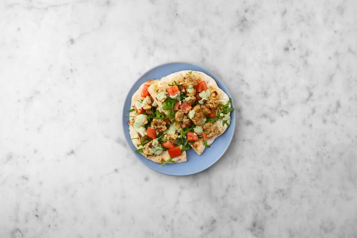 a) When everything's ready, share the toasted naans between your plates.
b) Top with the chermoula chicken and the rocket and tomato salad.
c) Drizzle over the zhoug yoghurt to finish.