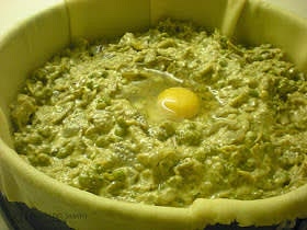 Come devi fare: metti in una terrina i piselli ed i carciofi ormai freddi, aggiungi 4 uova, il parmigiano, la ricotta, la maggiorana mescola bene il tutto ed aggiusta di sale. Prendi circa 2/3 della pasta violata e stendila con il mattarello per formare una bella sfoglia rotonda, il più possibile sottile e grande in modo da coprire il fondo ed i bordi, con un po' di abbondanza, di una teglia di 24 cm di diametro (meglio a cerchio apribile). Prendi la sfoglia, arrotolandola per metà la sul mattarello, e stendila con delicatezza nella teglia, fai in modo che tocchi bene il fondo e forma delle pieghe sulla parte del bordo per foderare bene tutta la teglia.
Stendi la pasta rimanente in una sfoglia di pari spessore ma un po' più piccola.
Riempi la torta con il ripieno, crea al centro un piccolo fosso nel quale metterai un uovo crudo. Ricopri con la seconda sfoglia facendola aderire al ripieno ed unisci le due sfoglie schiacciando per bene per attaccare le due parti ed assottigliare il bordo. Togli il cerchio dalla teglia e, con le forbici, taglia l'eccedenza di pasta in modo da ottenere un bordo, formato dalle due sfoglie unite, alto circa 1,5 cm. Ripiega il bordo arrotolandolo su se stesso in modo da formare un “cordino” oppure schiaccialo con i rebbi di una forchetta facendo attenzione a non bucare la pasta.
Cuoci in forno preriscaldato a 200 gradi per circa ½ ora, la pasqualina deve essere leggermente dorata. Lasciala raffreddare prima di servirla.