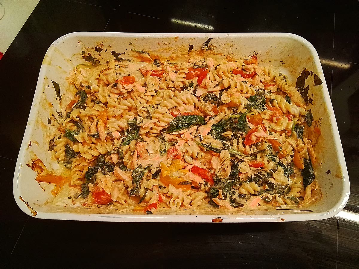 Wenn die 15 Minuten um sind, holen wir die Auflaufform aus dem Backofen. Als erstes nehmen wir die Knoblauchknolle aus der Form und legen sie beiseite. Wir entfernen den Lachs von der Haut und entsorgen diese. Die Knolle drücken wir aus, zerdrücken die weichen Zehen, fügen die Pasta hinzu und vermengen alles. Beim Vermengen noch die Gewürze nach Wahl hinzufügen und mitvermengen.