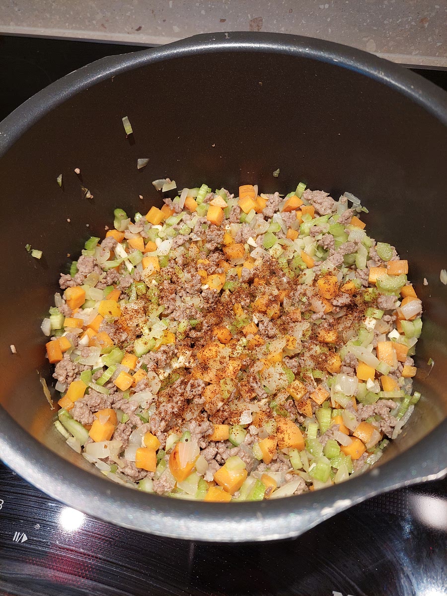 When the meat has just fully browned, pour it into the pot. Finely chop the cloves of garlic and add it to the pot. Add the celery and chilli powder now too. Stir occasionally and keep frying for another 5 minutes. This is a good time to clean the cutting board.