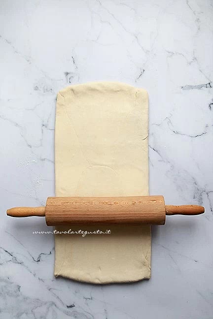 Poi spolverate con un pizzico di farina il vostro quadrato e il piano di lavoro e con l’aiuto di mattarello stendete il quadrato allungandolo in un rettangolo ad uno spessore di 1,5 cm di spessore