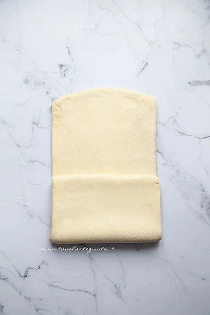 A questo punto piegare a portafoglio, ovvero ripiegare sul centro del rettangolo la terza parte del rettangolo più vicina a sé e premerla leggermente col mattarello: