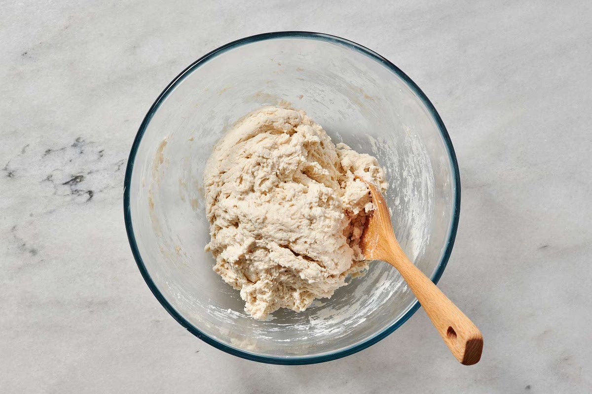 Make a well in the middle of your dry ingredients and add the wet mixture to your dry mixture kneading using a large wooden spoon, transferring to the counter once it comes together.